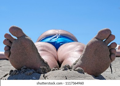 Close Up The Foot Of The Sunbathing Fat Man Photographed In A Comical Foreshortening