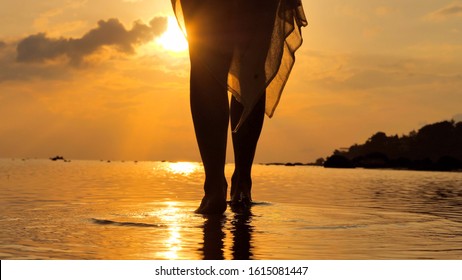 Close up at  foot of young woman walking in at seashore  wearing a long flowing dress as sunset time in the distance - Powered by Shutterstock