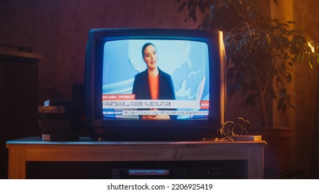 Close Up Footage Of A Dated TV Set Screen With Breaking News Report. Beautiful Female Host Reads Important News On Live Television Broadcast. Nostalgic And Retro Nineties Technology Concept.