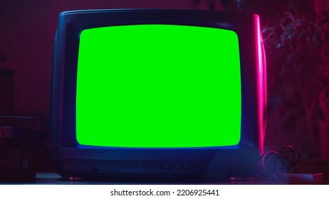 Close Up Footage Of A Dated TV Set With Green Screen Mock Up Chroma Key Template Display. Nostalgic Retro Nineties Technology Concept. Vintage Television Display In Neon Lit Living Room.