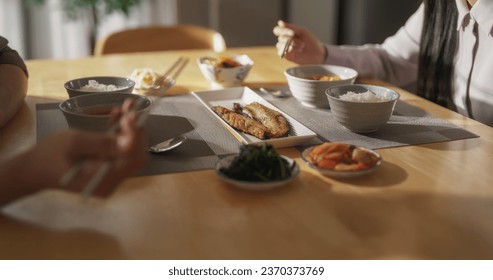 Close Up Footage Focusing on Tasty Dishes on a Dining Table with Rice Bowls, Spicy Asian Soup, Fish and Vegetables. Young Asian Man and Woman Having a Korean Lunch at Home in the Kitchen - Powered by Shutterstock