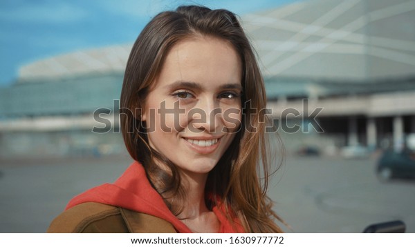 Close up footage of nice\
young woman looking directly at camera, holding black smartphone in\
hand. Natural beauty. Caucasian. Contemporary architecture in\
background.