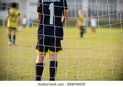 Close up of football goal net, seeing a young soccer goalie goalkeeper during the match. Youth Soccer game on a sunny summer school tournament Day. Football match going on in a background. - Powered by Shutterstock