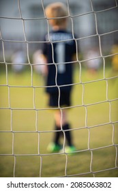 Close Up Football Goal Net, Seeing A Young Boy Soccer Goalkeeper Watching His Teammate Playing. Youth Soccer Game On A Sunny Summer School Tournament Day. A Football Match Going On In A Background.