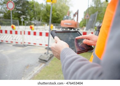 Close Up Of Foremans Hands Using Digital Tablet On Road Construction Site