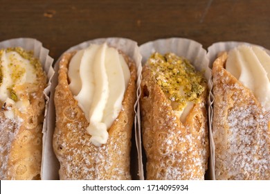 Close up of four cannoli freshly display in nice paper on a wooden background