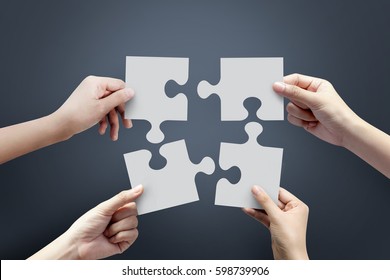 Close Up Of Four Hands Holding Jigsaw, Concept For Teamwork Building A Success.