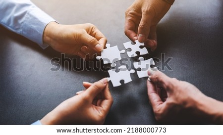 Close up four hands holding pieces of white jigsaw puzzle, joint path to problem solution, find way out exit of difficult situation. Support, teamwork concept.