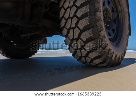 Close up of a four-wheel drive's tyre on the sandy beach - coastline