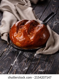 Close Up Of Fragrant Baked Homemade Bread On Dark Wooden Table. Fragrant Round Bread With Brown Crust Lies On Frying Pan Near Gray Cloth. Concept Of Bakery Products.