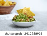 Close up of fresh avocado guacamole dip with salted tortilla chips in wooden bowl in background, grey marble table