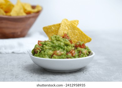 Close up of fresh avocado guacamole dip with salted tortilla chips in wooden bowl in background, grey marble table