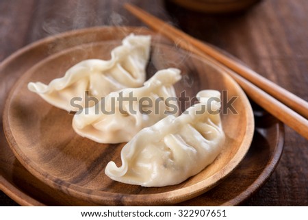 Close up fresh boiled dumplings with hot steams on wood plate. Chinese food on rustic old vintage wooden background. 