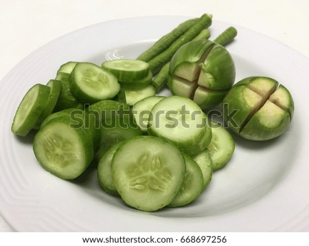 Close up of fresh cucumber, green bean and Thai eggplants on a white plate and white background. They are sliced, cut and ready to be served. Thai people eat fresh vegetables with spicy dipping sauce.