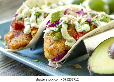 Close up of fresh fish tacos with coleslaw, avocado, salsa and lime creme in a flour tortilla on blue plate