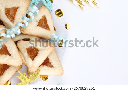 Close up freshly baked triangular cookies, adorned with light blue ribbons and decorated mask on a white table. Purim celebration concept. space for text. High quality photo