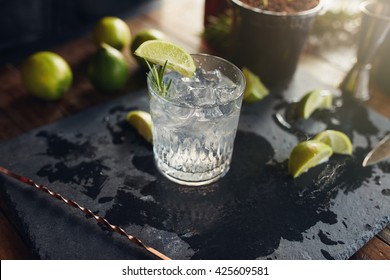 Close up of freshly made gin and tonic drink with lemon slices and spoon on a black board.