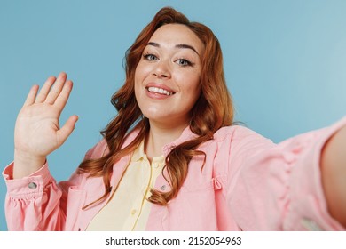 Close Up Friendly Young Redhead Chubby Overweight Woman 30s In Pink Shirt Doing Selfie Shot On Mobile Phone Waving Hand Isolated On Pastel Blue Background Studio Portrait. People Lifestyle Concept.