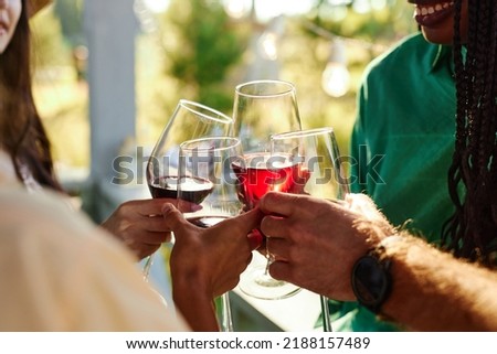 Close up of friends toasting with wine glasses in celebration during outdoor party in Summer