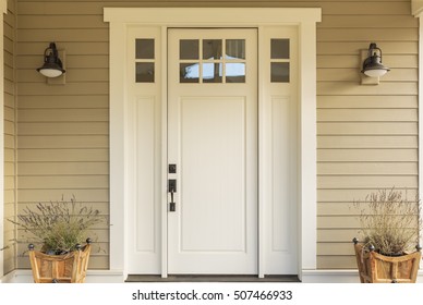 Close up of a front door with small square decorative windows and flower pots