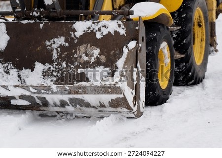Close up of front loader bucket and large rubber tires covered with snow showing heavy construction machinery operating in winter worksite conditions