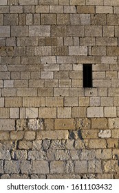 Close up front outdoor view of part of a beige white stone wall with a small opening, northern France. Abstract design with pattern of rectangular blocks and lines. Ancient masonry facade.