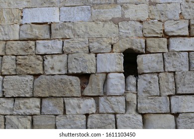 Close up front outdoor view of part of a beige white stone wall with a small opening, northern France. Abstract design with pattern of rectangular blocks and lines. Ancient masonry facade.