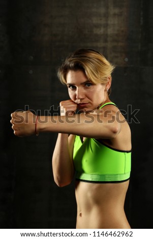 Similar – Close up front portrait of one young athletic woman in sportswear in gym over dark background, standing in boxing stance with hands and fists, looking at camera