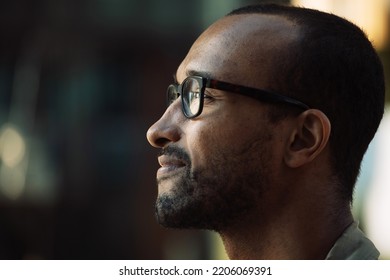 Close up front portrait of serious young African man wearing eyeglasses with serious expression in the city, side view - Powered by Shutterstock