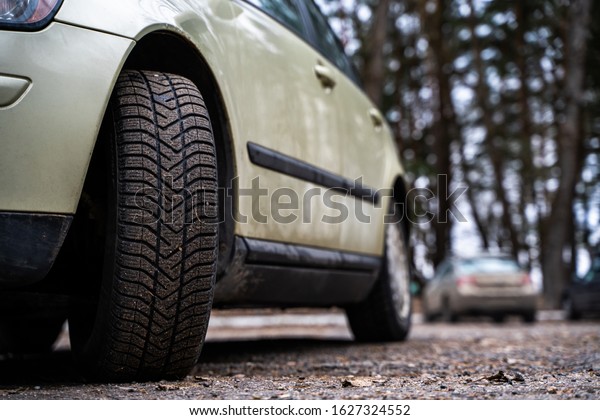 Close up\
front view of a family car on parking with another cars on\
background. Dirty front wheel tire on asphalt.\
