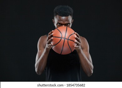 Close up front view shot of afro american male basketball player holding a ball in front of him over black background - Powered by Shutterstock