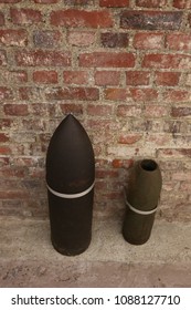 Close up front view of two ancient shells used during the world war I. Metallic explosive objects exposed in front of a red bricks wall. Vintage design. Abstract symbolic view of danger. 
