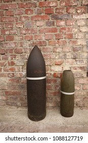 Close up front view of two ancient shells used during the world war I. Metallic explosive objects exposed in front of a red bricks wall. Vintage design. Abstract symbolic view of danger. 