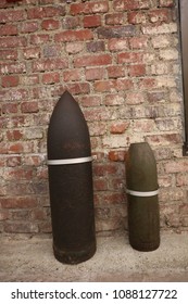 Close up front view of two ancient shells used during the world war I. Metallic explosive objects exposed in front of a red bricks wall. Vintage design. Abstract symbolic view of danger. 