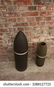 Close up front view of two ancient shells used during the world war I. Metallic explosive objects exposed in front of a red bricks wall. Vintage design. Abstract symbolic view of danger. 
