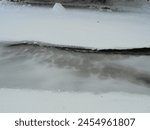 Close up : Frozen Ostravice river in Czech mountains covered by a layer of cracked partially transparent ice and snow during snowy winter day