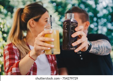 Close up fruit and vegetable detox diet juice in plastic bottles concept. Couple holding bottles with fresh organic juice. Garden, outdoor - Powered by Shutterstock