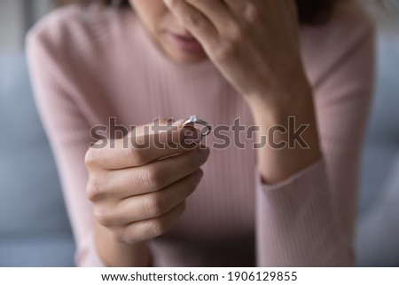 Close up frustrated millennial unhappy desperate woman holding engagement ring with diamond in hand, suffering from relations breakup or fiancee betrayal, denied marriage or getting divorced.