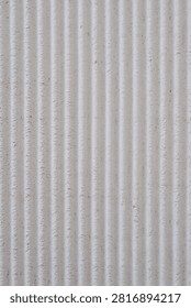 A close up full frame shot of a rough textured concrete wall surface featuring uniform vertical linear grooves.