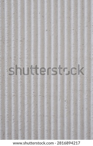 A close up full frame shot of a rough textured concrete wall surface featuring uniform vertical linear grooves.