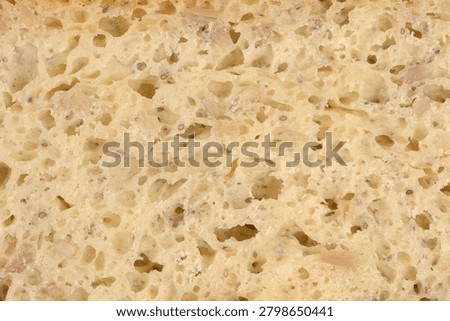 A close up full frame view of the soft crumb texture of sliced white sandwich bread mixed with small grains and sunflower seeds