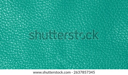 A close up full frame view of a vibrant teal colored leather texture, showcasing its natural grain