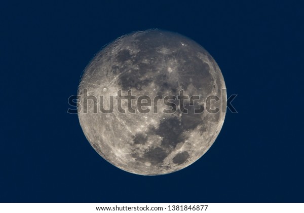 Close up of full moon against Blue sky featuring
moon craters and seas