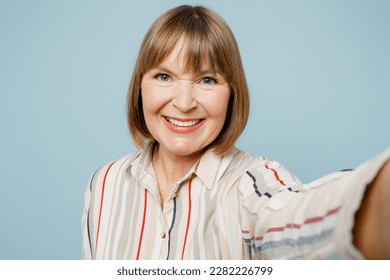 Close up fun elderly woman 50s years old wearing light striped shirt doing selfie shot pov on mobile cell phone isolated on plain pastel blue cyan color background studio portrait. Lifestyle concept - Powered by Shutterstock