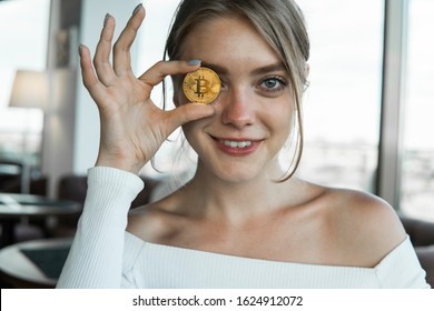 Close up fun emotional young female is holding bitcoin in front eye. Online virtual future currency concept. Beauty woman head with Bitcoin money in eye. Digital cryptocurrency bitcoin.
