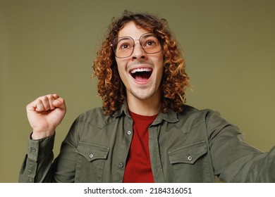 Close Up Fun Young Brunet Curly Man 20s Wears Khaki Shirt Do Selfie Shot Pov On Mobile Phone Winner Gesture Celebrate Clenching Fists Say Yes Isolated On Plain Olive Green Background Studio Portrait