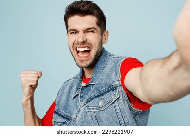 Close up fun young caucasian man he wears denim vest red t-shirt casual clothes doing selfie shot pov on mobile cell phone do winner gesture isolated on plain pastel light blue cyan background studio - Powered by Shutterstock