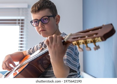 Close up funny boy with glasses learns to play the classical guitar at home.
