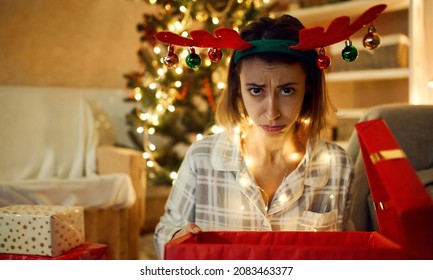 Close Up Funny Frowns Face Of Festive X-mas Woman. Disappointed Woman With Opened Bad Christmas Gift Box At Home