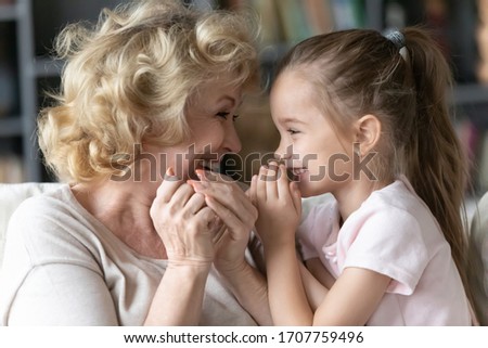 Close up of funny grand daughter joyful grandmother telling secrets each other gossiping sitting on sofa in living room at home, multi-generational family trusted relations, strong connections concept